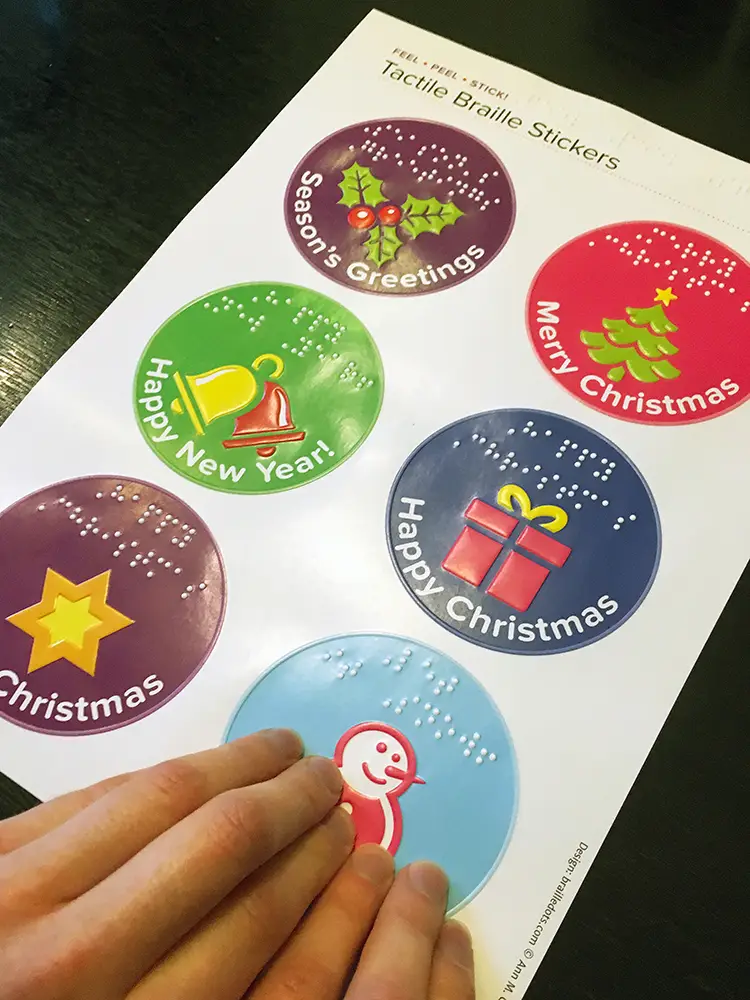 A blind woman feeling the illustrations on the sticker sheet and reading the festive messages in braille.