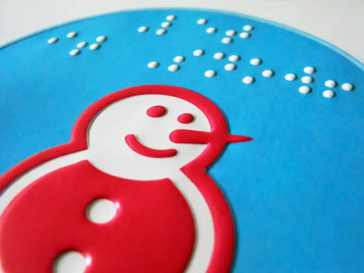 Blue sticker with festive message in braille and large type and a tactile illustration of a snowman in pink and white.